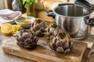 Artichauts cuits à la cocotte-minute posés sur une planche en bois avec citron et vinaigrette